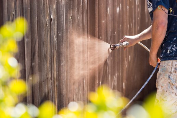 Professional Painter Spraying House Yard Fence with Wood Stain.