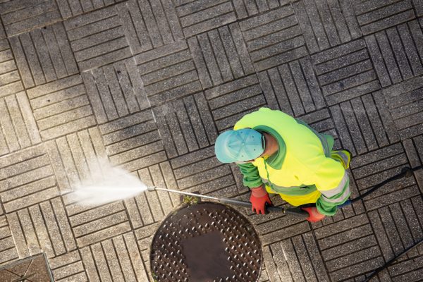 Worker cleaning a street sidewalk with high pressure water jet machine on sunny day. Copy space. Top view